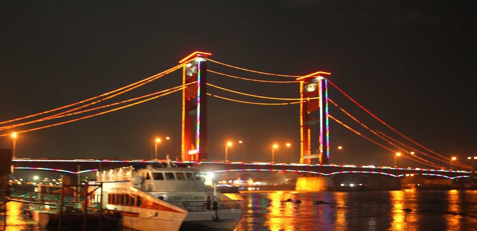 Jembatan Ampera di malam hari dengan pantulan cahaya di Sungai Musi