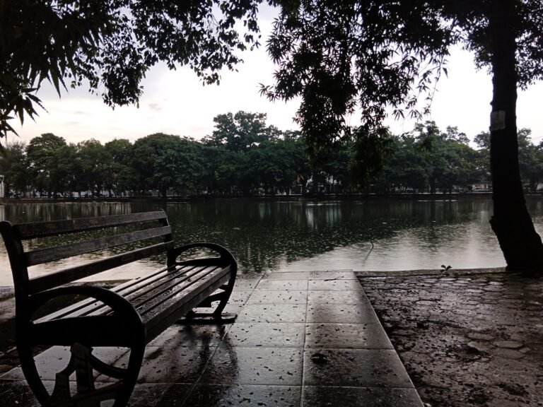 Danau Taman Kambang Iwak Palembang dengan bangku taman di tepi air saat hujan